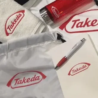 Artículos promocionales: fotografía de una bolsa, tarjetas y un termo en color blanco con rojo hechas con tampografía.