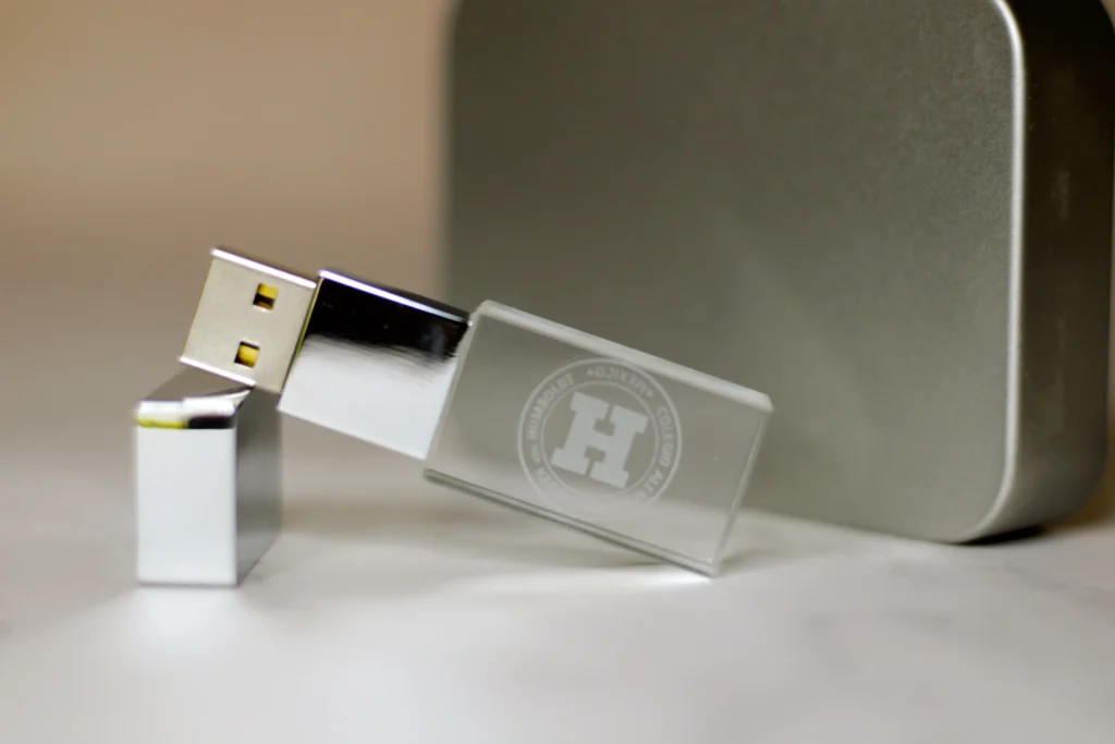 Fotografía de una memoria USB color plateado con un logotipo color blanco hecho con grabado láser sobre una mesa.