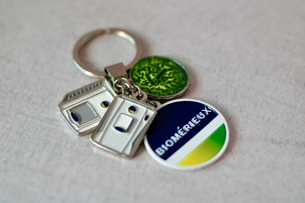 Fotografía de un llavero redondo color blanco con azul y verde que tiene un logotipo hecho con grabado láser.
